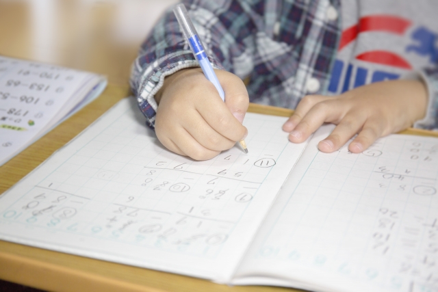 子供が鉛筆で学習ノートに文字を書く練習をしている、書き取りの練習をしているイメージ画像。