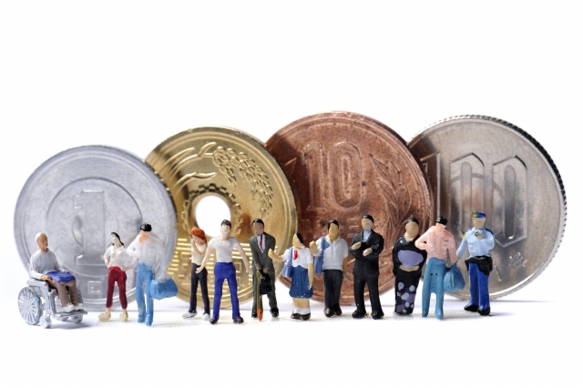 コインの前で様々な人のミニチュアが並んで列をなしているお金にまつわるイメージ画像。情報にもバリアフリーを。障がい者とその関係者のコミュニティ、情報サイト。ナレバリ