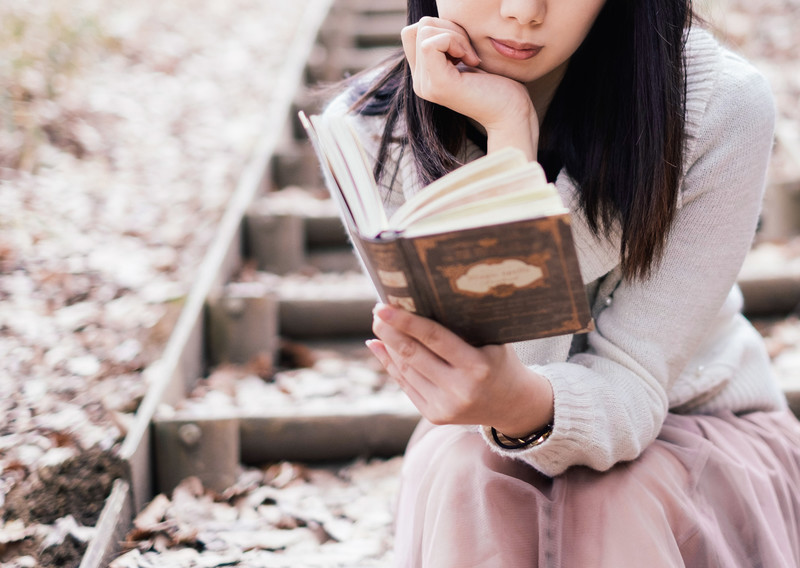 秋の枯れ葉が落ちる公園で読書を楽しむ女性のイメージ画像。情報にもバリアフリーを。障がい者とその関係者のコミュニティ、情報サイト。ナレバリ