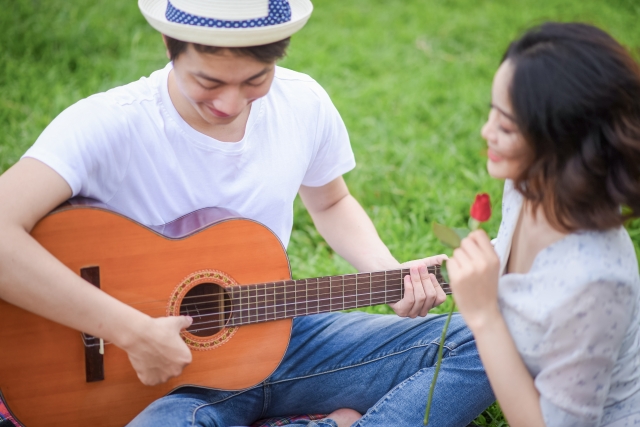 ピクニックでギターを弾いて歌を歌って楽しんでいる男女のイメージ。