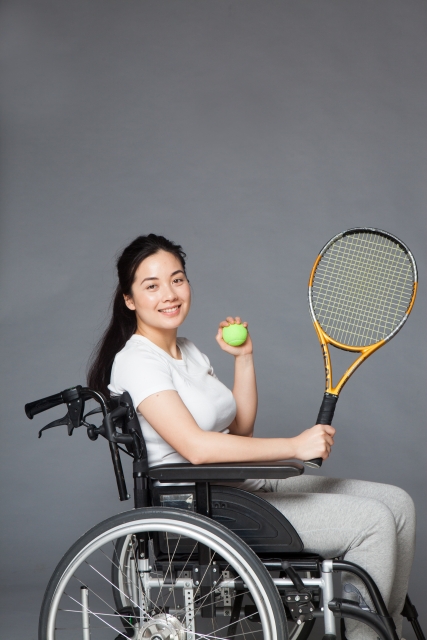車いすテニスにチャレンジしようとしている笑顔の女性の明るくてさわやかで活動的な画像。情報にもバリアフリーを。障がい者とその関係者のコミュニティ、情報サイト。ナレバリ