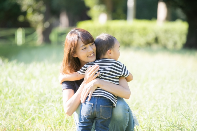 2歳の子供と公園で遊んでいる中で愛情をもって優しく抱きかかえるお母さんのイメージ。情報にもバリアフリーを。障がい者とその関係者のコミュニティ、情報サイト。ナレバリ